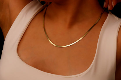 A close-up image of a person wearing a 14K gold herringbone snake chain necklace.
