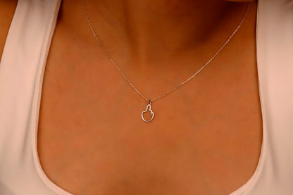 A close-up image of a person wearing a tiny middle finger-shaped necklace in silver, with hands adjusting the necklace.
