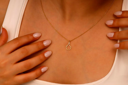 A close-up image of a person wearing a tiny middle finger-shaped necklace in silver, with hands adjusting the necklace.