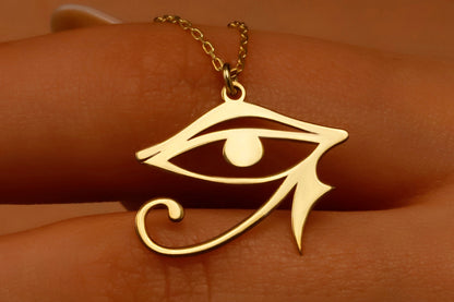 A gold-colored Eye of Ra necklace displayed on a person's hand, featuring a dainty pendant with intricate details.