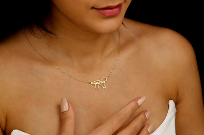 A woman is seen from the shoulders up, wearing a custom dog name necklace with a pet silhouette design. The necklace is gold-colored, and the pendant features a dog's silhouette with a letter.