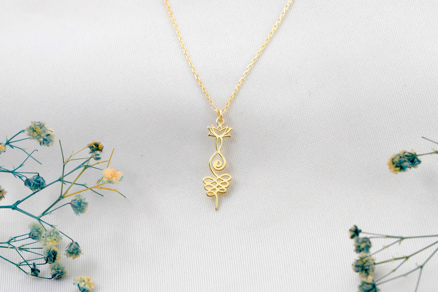 Gold necklace with a intricate pendant on a light gray background with dried flowers.