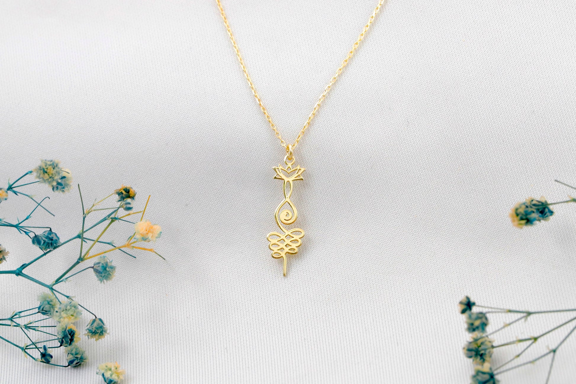 Gold necklace with a intricate pendant on a light gray background with dried flowers.