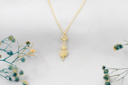 Gold necklace with a intricate pendant on a light gray background with dried flowers.