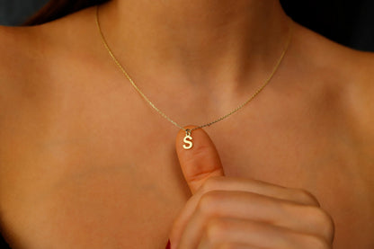 A close-up image of a person wearing a gold initial necklace with the letter 'S'.