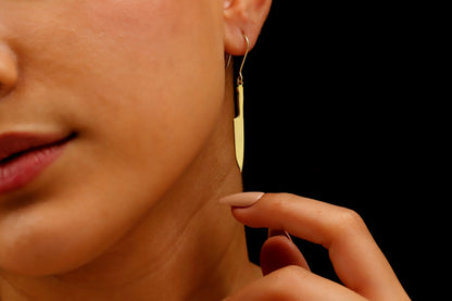 A close-up image of a person wearing a silver knife earring with a gold-filled dagger earring in their ear.