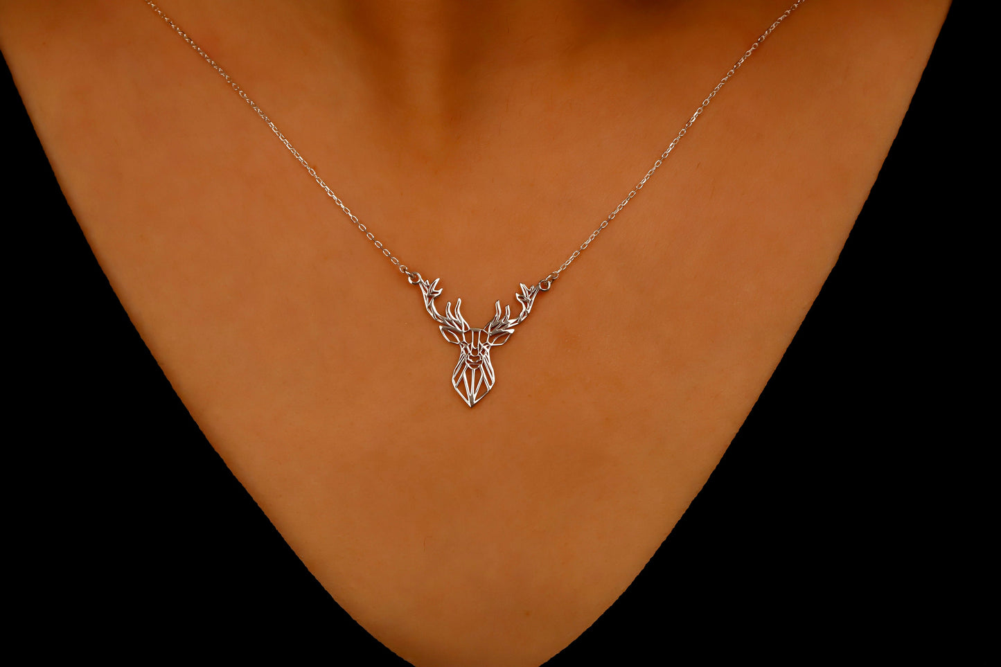 Necklace with a deer pendant on a person's neck against a dark background