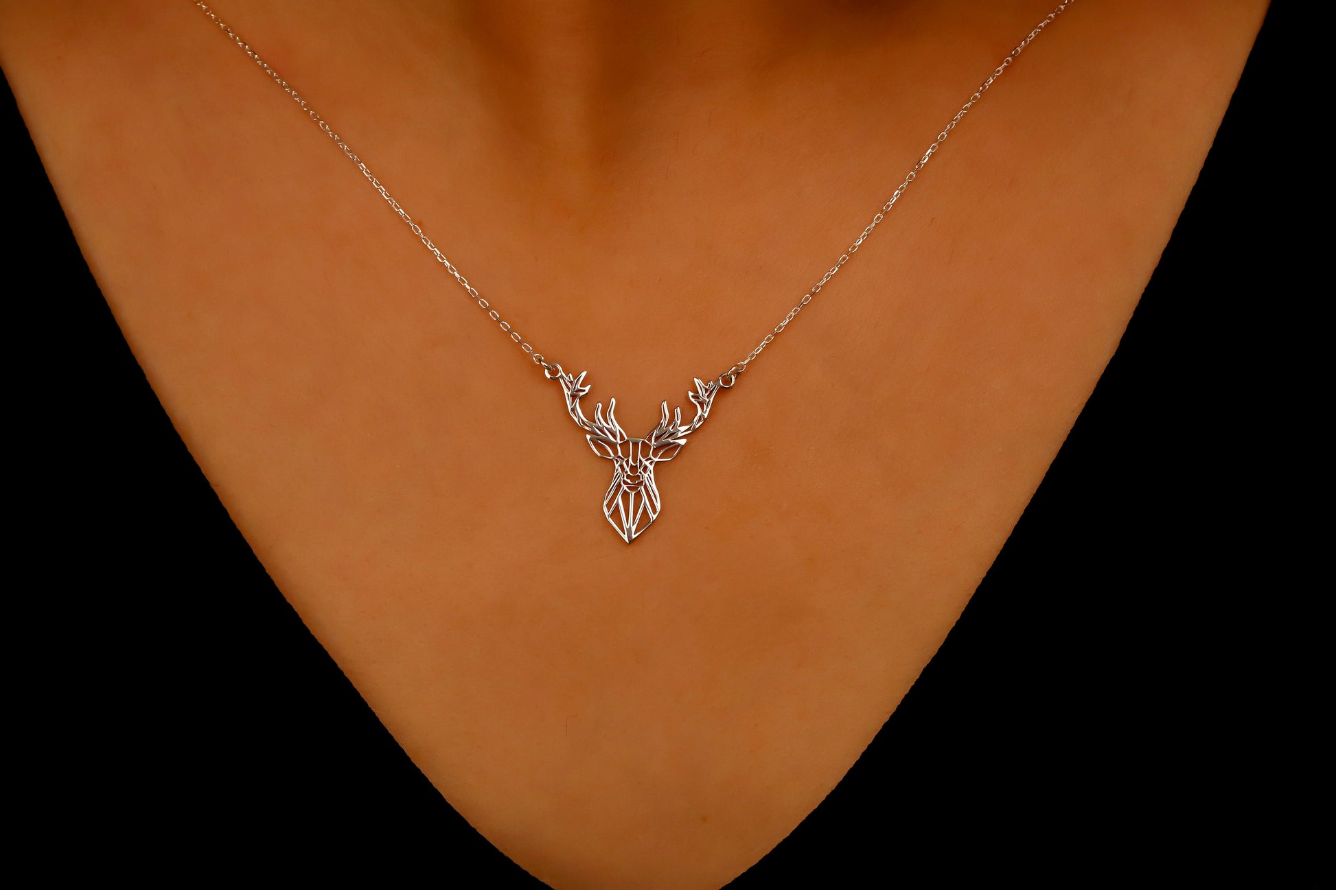 Necklace with a deer pendant on a person's neck against a dark background