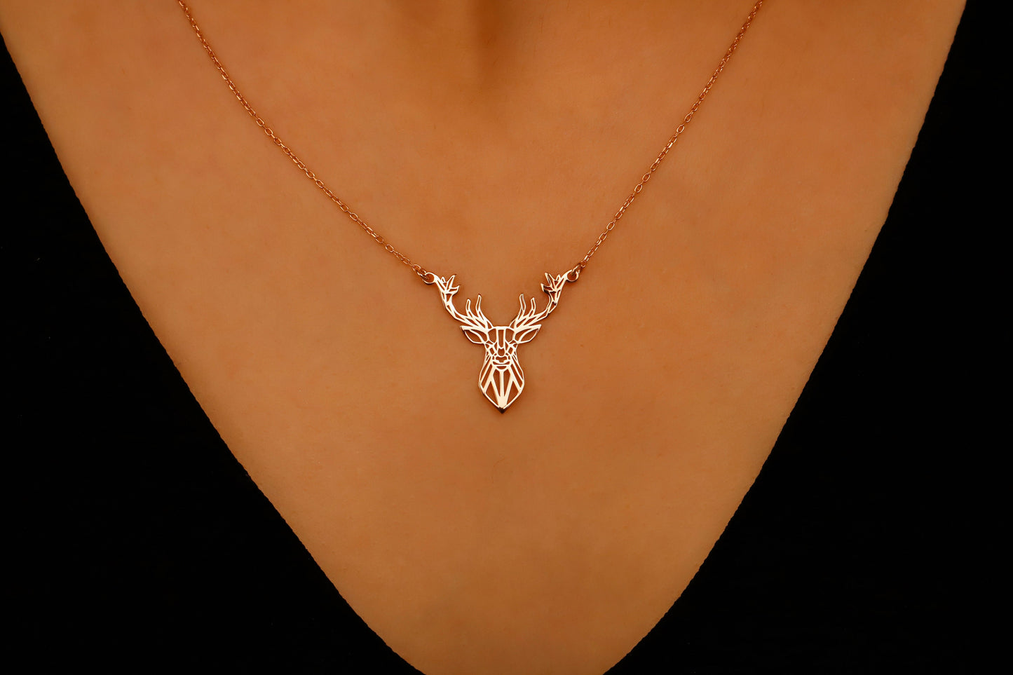 Gold deer head necklace on a person's neck against a black background