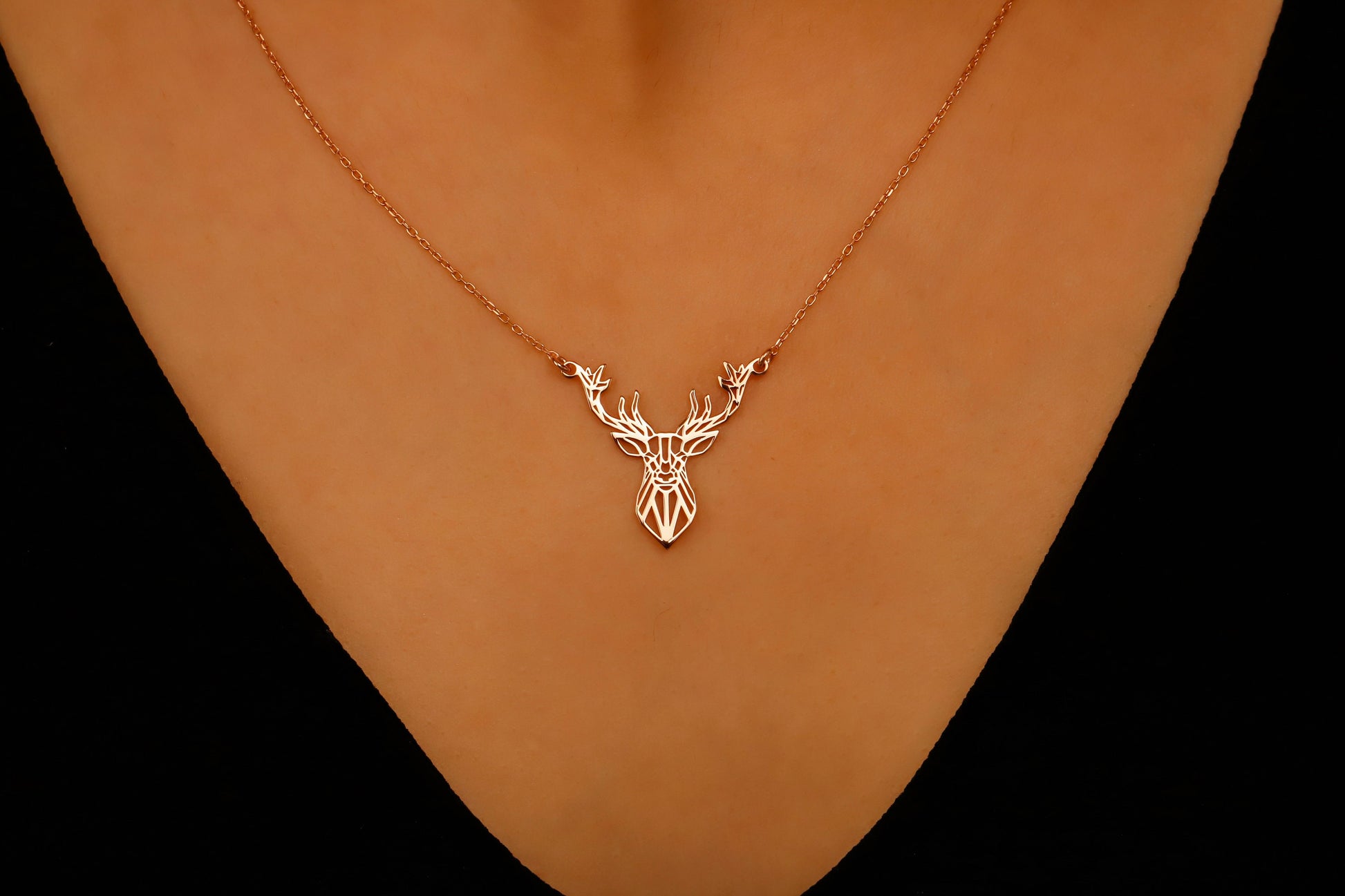 Gold deer head necklace on a person's neck against a black background