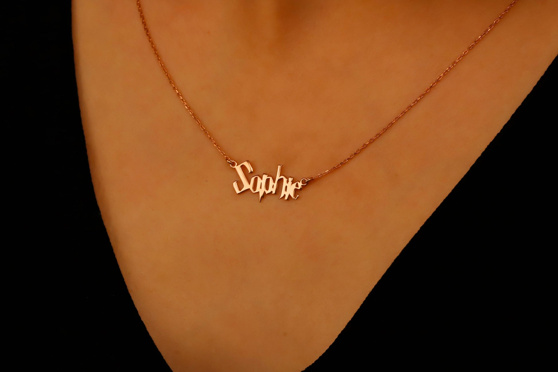 Gold necklace with 'Sophie' pendant on a person's neck against a black background