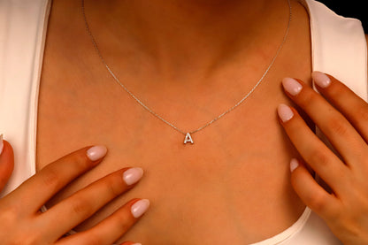 Person wearing a silver necklace with a 'A' pendant, hands touching the chest.