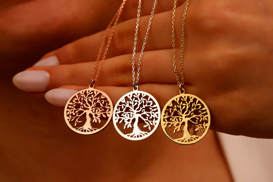 A woman's hands adjusting 3 delicates necklaces with a Tree of Life pendant in gold rose and rose