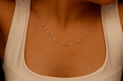 A close-up image of a silver Singapore chain necklace being held by a person's hands.