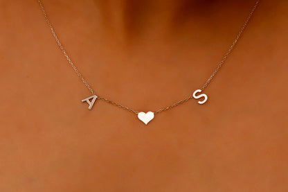 A woman wearing a delicate minimalist necklace with initial letters and a heart charm.
