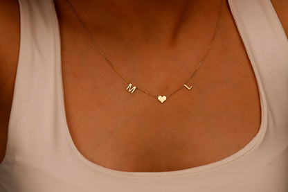 A woman wearing a white tank top showcasing a delicate minimalist necklace with initial letters and a heart charm.