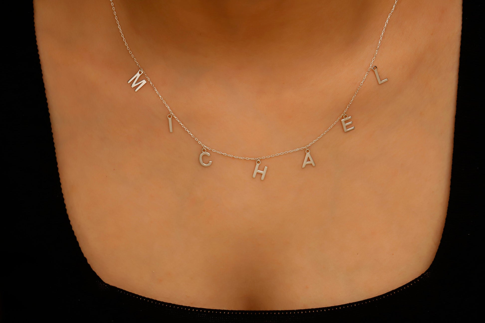 Necklace with 'MICHAEL' pendant on a person's neck against a black background
