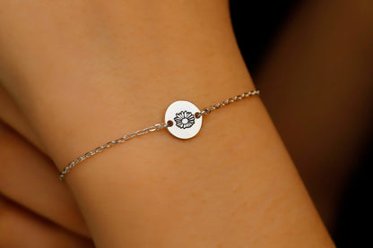 Silver bracelet with a circular charm on a wrist against a blurred background