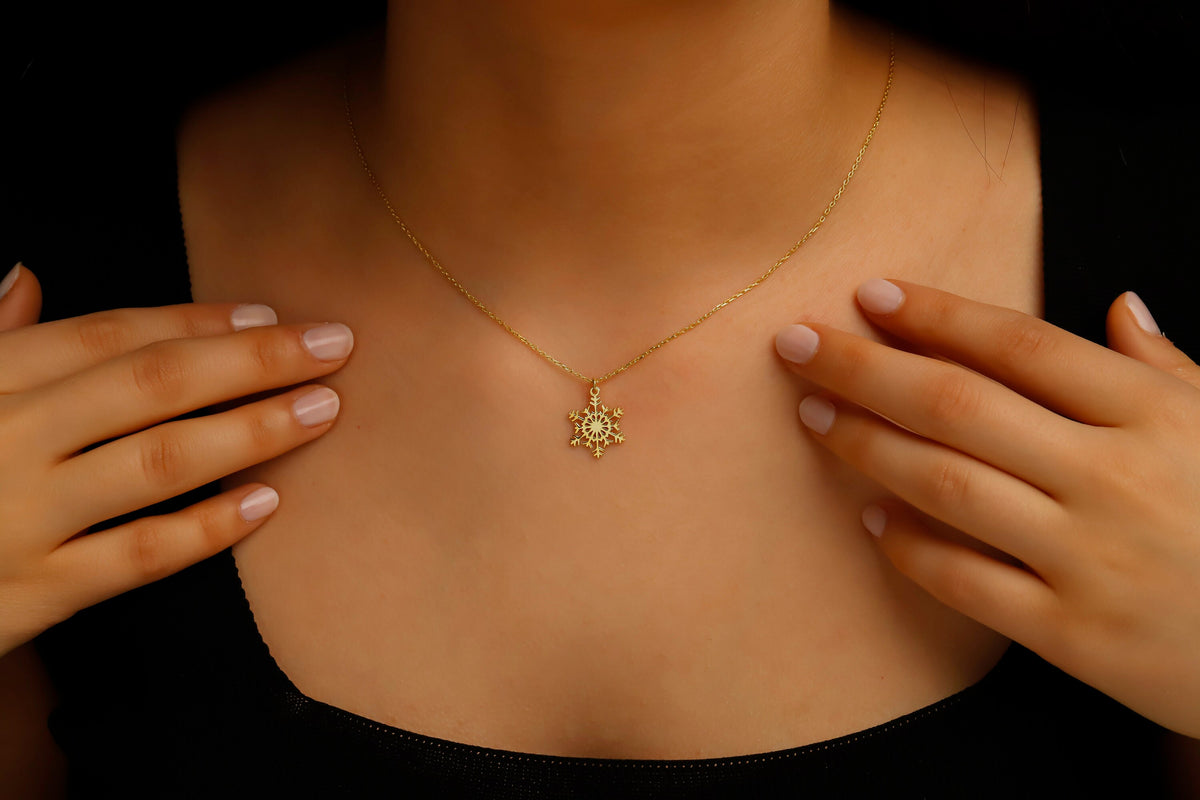 Gold necklace with a sunflower pendant worn by a person against a dark background