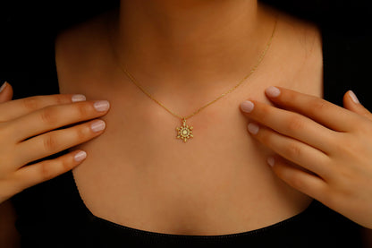 Gold necklace with a sunflower pendant worn by a person against a dark background