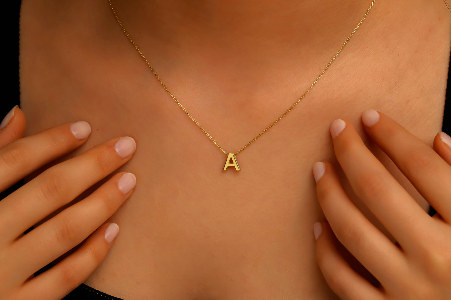 Gold necklace with a 'A' pendant on a person's chest.
