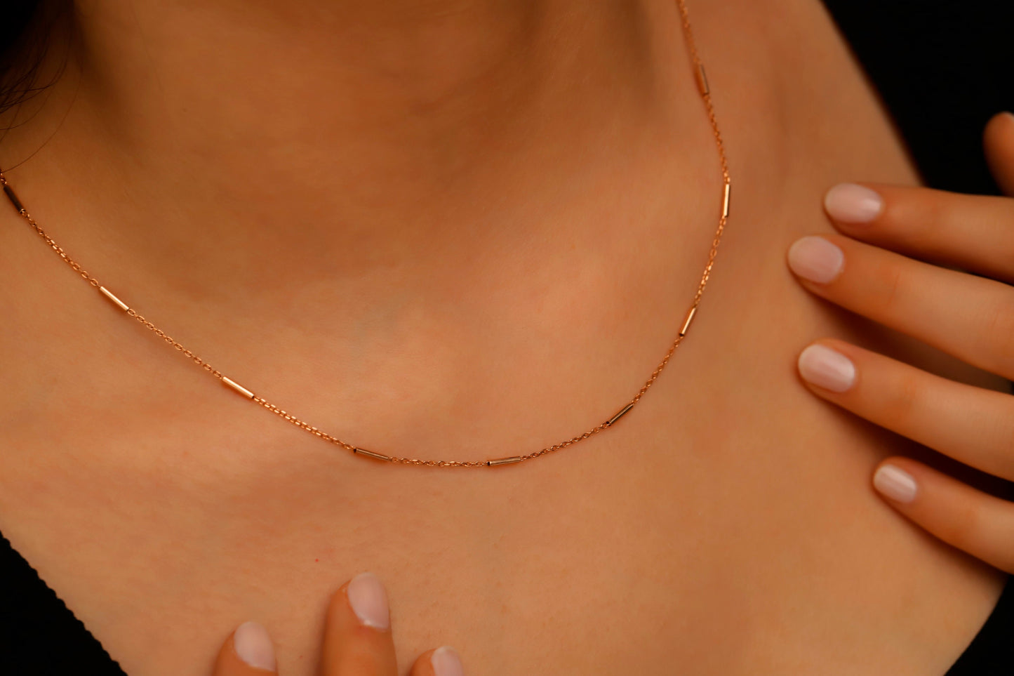 Rose gold necklace on a person's neck with a hand touching the skin.