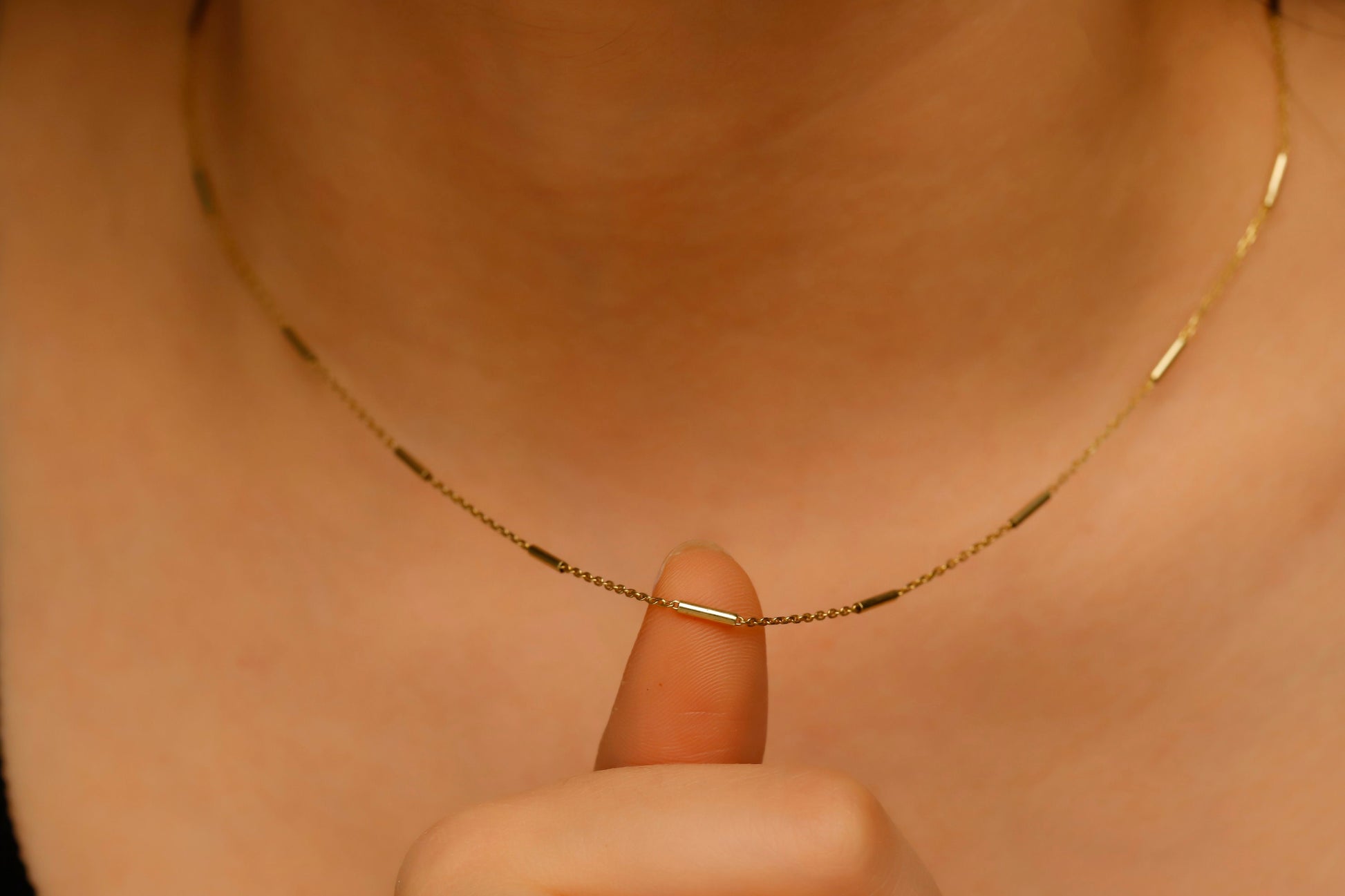 Gold necklace being held by a finger against a neutral background