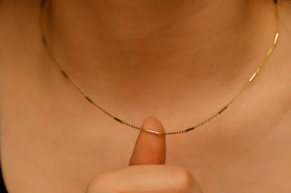Gold necklace being held by a finger against a neutral background