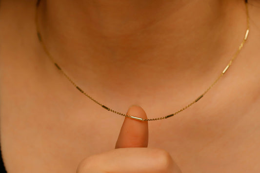 Gold necklace being held by a finger against a neutral background