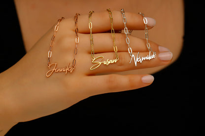 Gold name chain necklaces on a hand against a dark background