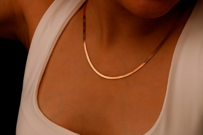 A close-up image of a person wearing a 14K rose gold herringbone snake chain necklace.