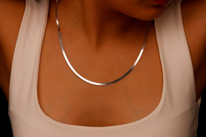 A close-up image of a person wearing a sterling silver herringbone snake chain necklace.