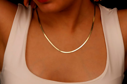 A close-up image of a person wearing a 14K gold herringbone snake chain necklace.