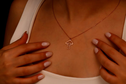 A close-up image of a person's hand holding a dainty gold necklace with a mushroom pendant.