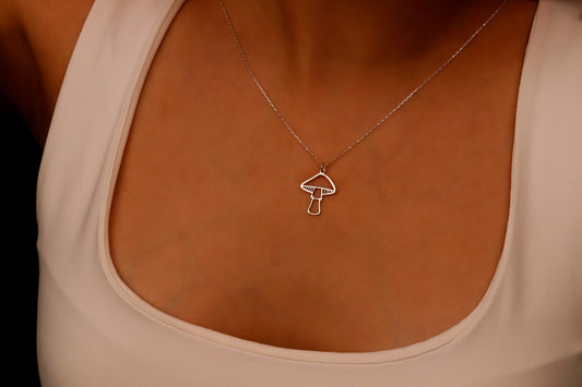 A close-up image of a person's hand holding a dainty gold necklace with a mushroom pendant.