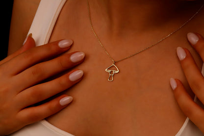 A close-up image of a person's hand holding a dainty gold necklace with a mushroom pendant.