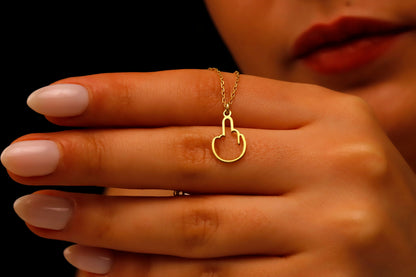 A close-up image of a person wearing a tiny middle finger-shaped necklace in silver, with hands adjusting the necklace.