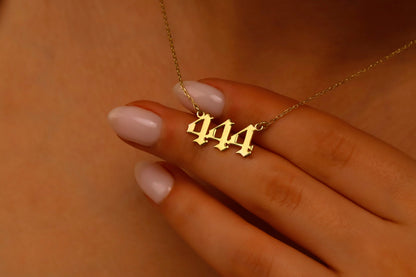 A close-up image of a necklace with the number 444 on a charm, held by a person with red nail polish.
