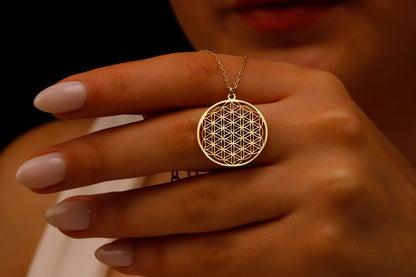 A gold pendant necklace featuring the Flower of Life design, held between a person's fingers.