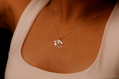 A gold-colored Eye of Ra necklace displayed on a person's hand, featuring a dainty pendant with intricate details.