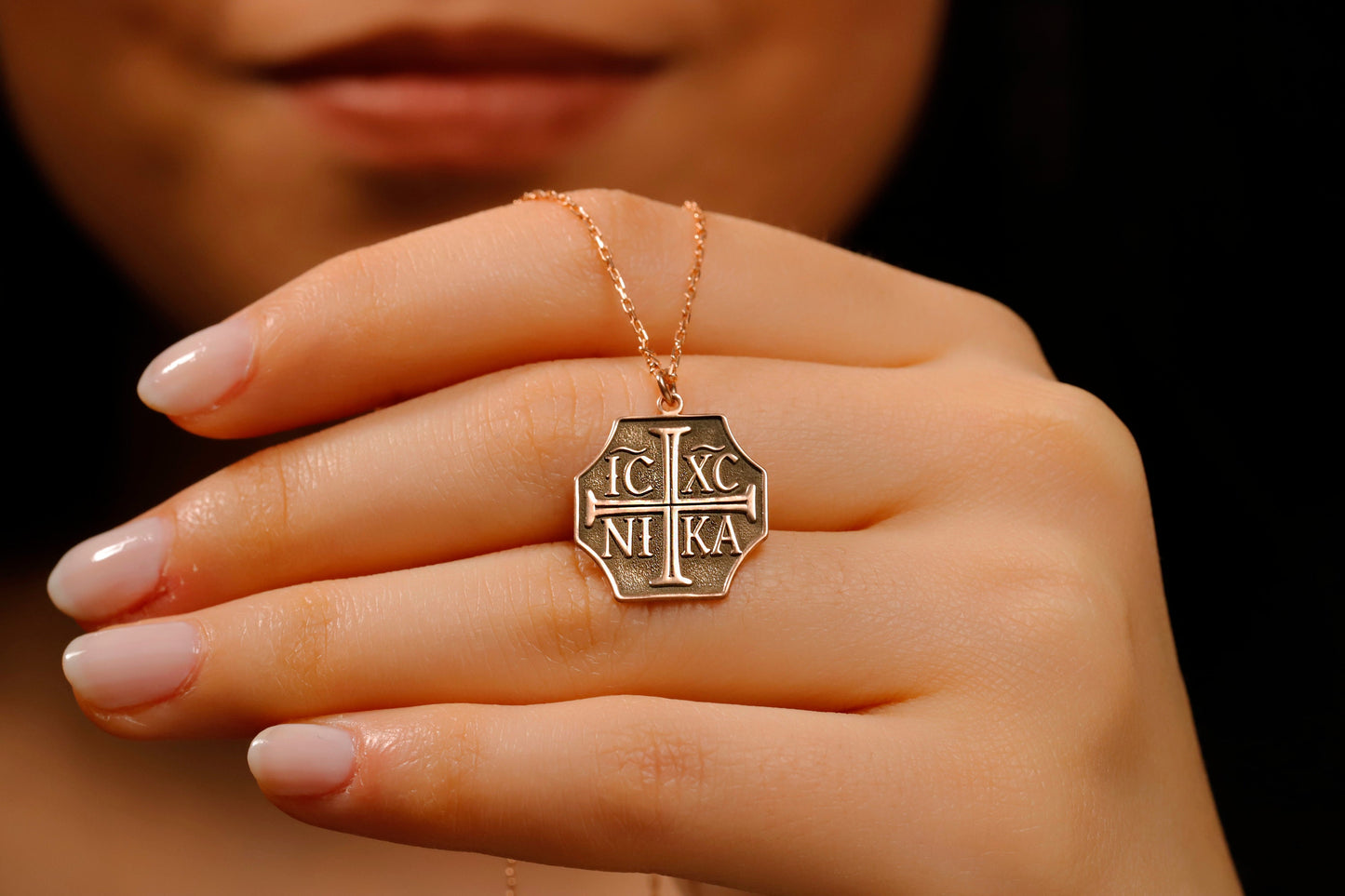 Gold necklace with a hexagonal pendant featuring symbols, held by a hand against a dark background.