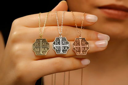 Three necklaces with religious symbols held by a hand against a blurred background