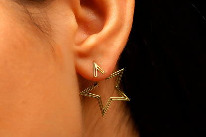 Gold star-shaped earring worn on an ear with a black background
