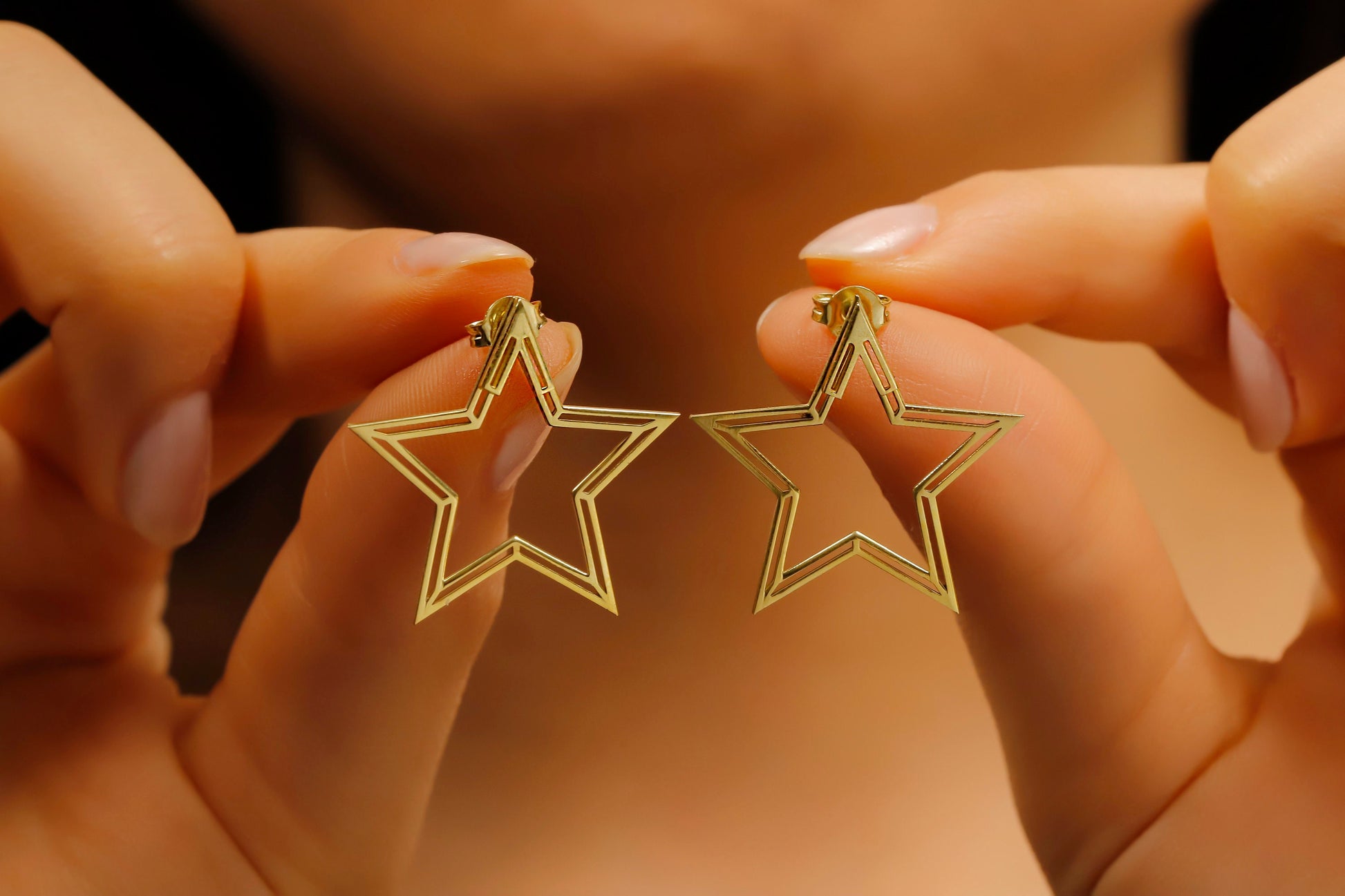 Gold star-shaped earrings held between fingers against a blurred background