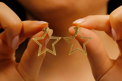 Gold star-shaped earrings held between fingers against a blurred background