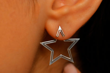 Silver star-shaped earring worn on an ear with a blurred background