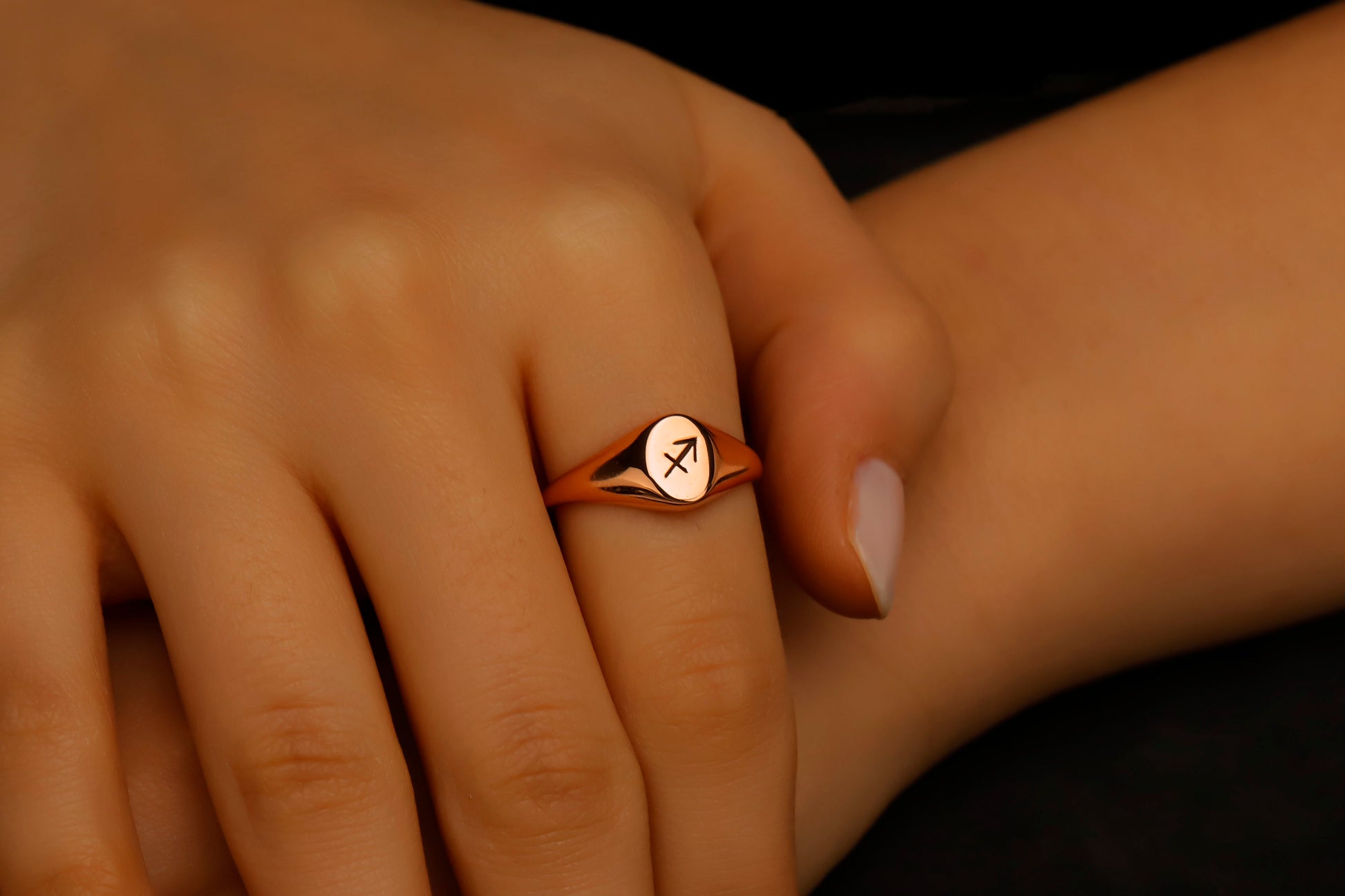 Rose gold ring with a symbol on a person's finger against a dark background