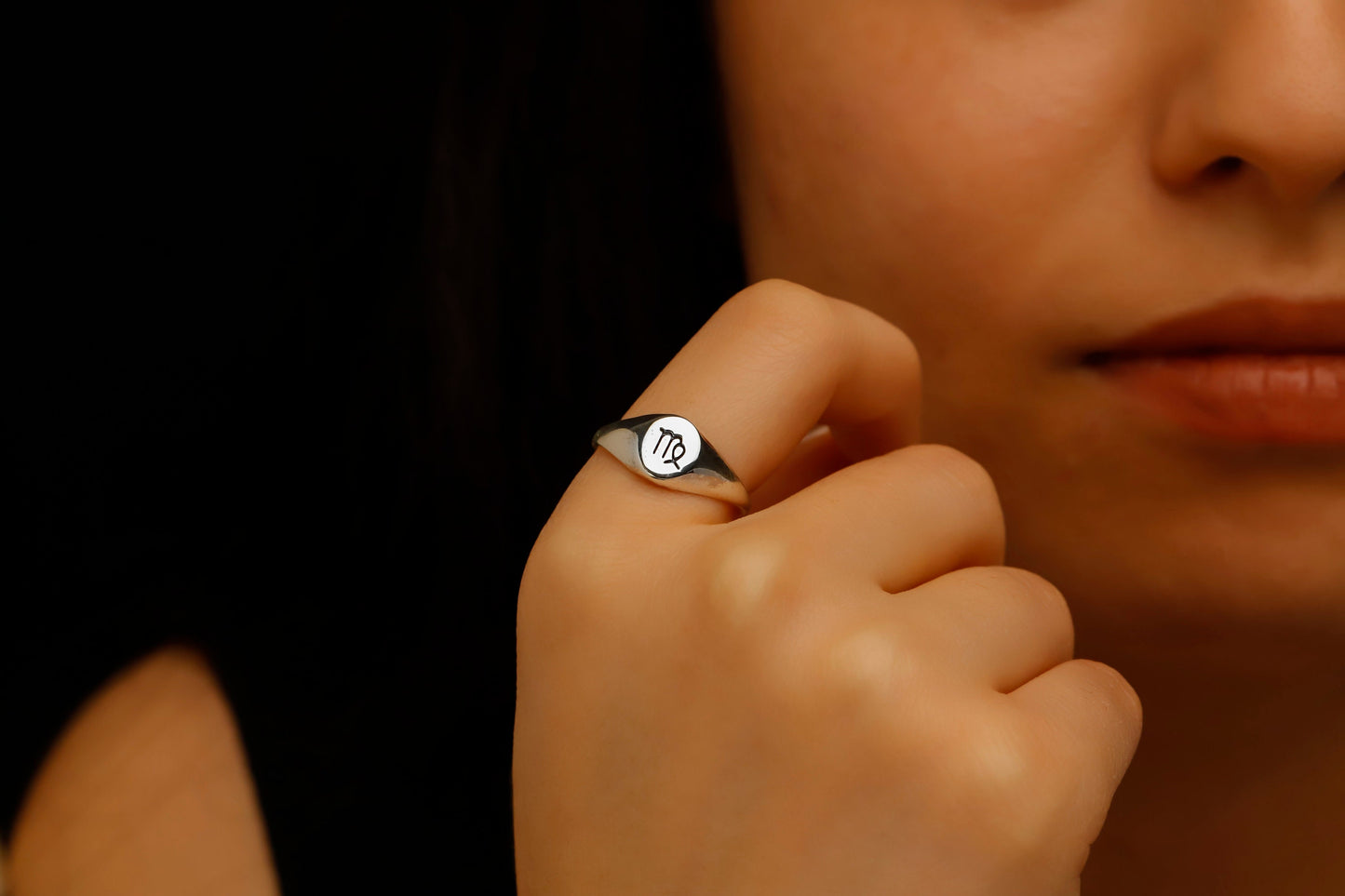 Close-up of a hand wearing a ring with a symbol, against a blurred background.