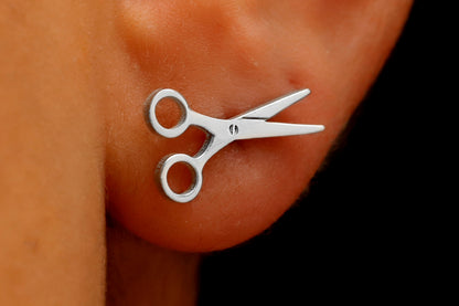 A close-up image of a person's ear wearing a small silver-colored scissor stud earring.