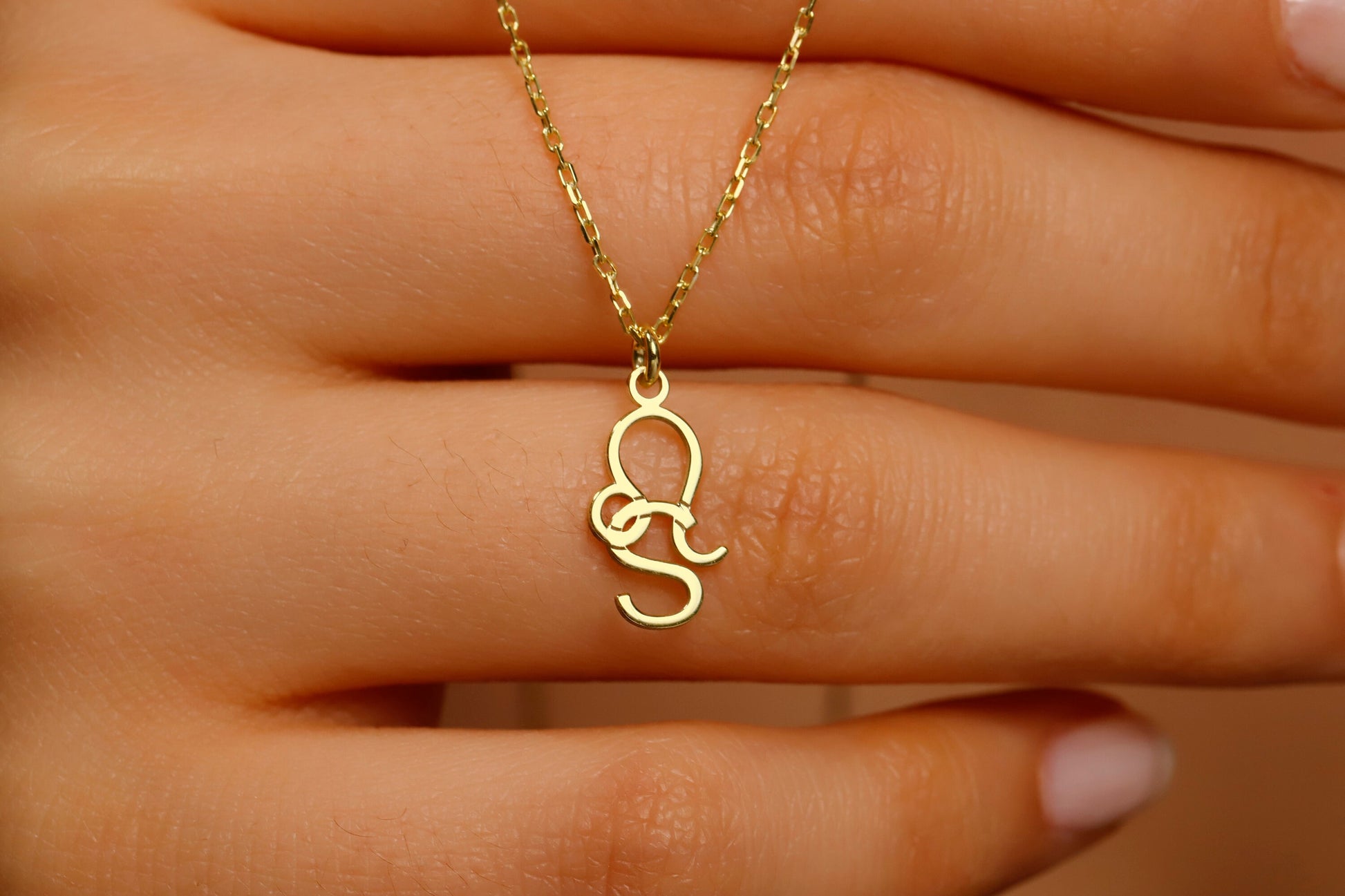 Gold necklace with a unique pendant held by a hand against a neutral background